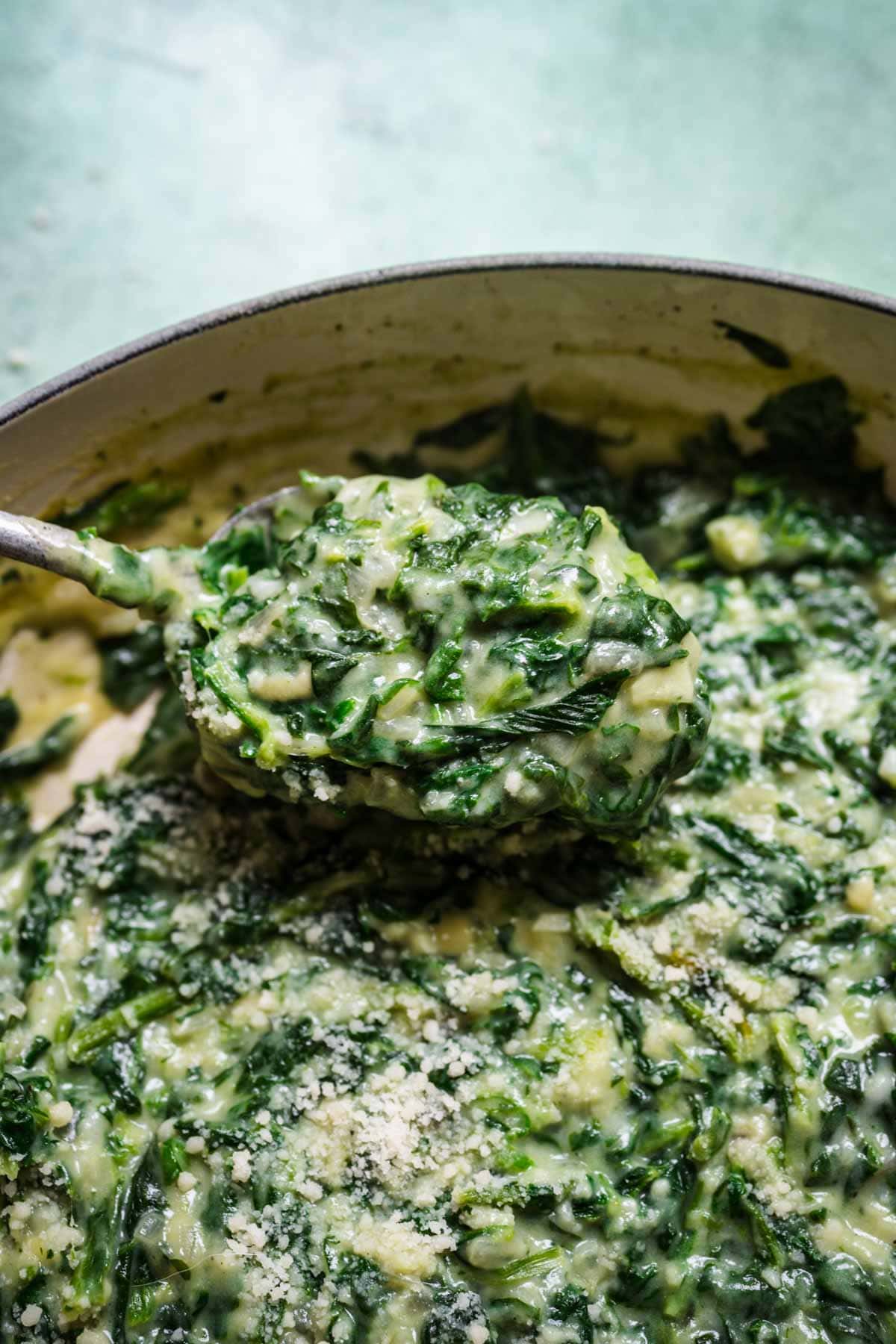 Close up of a spoonful of creamed spinach being scooped out of a bowl.