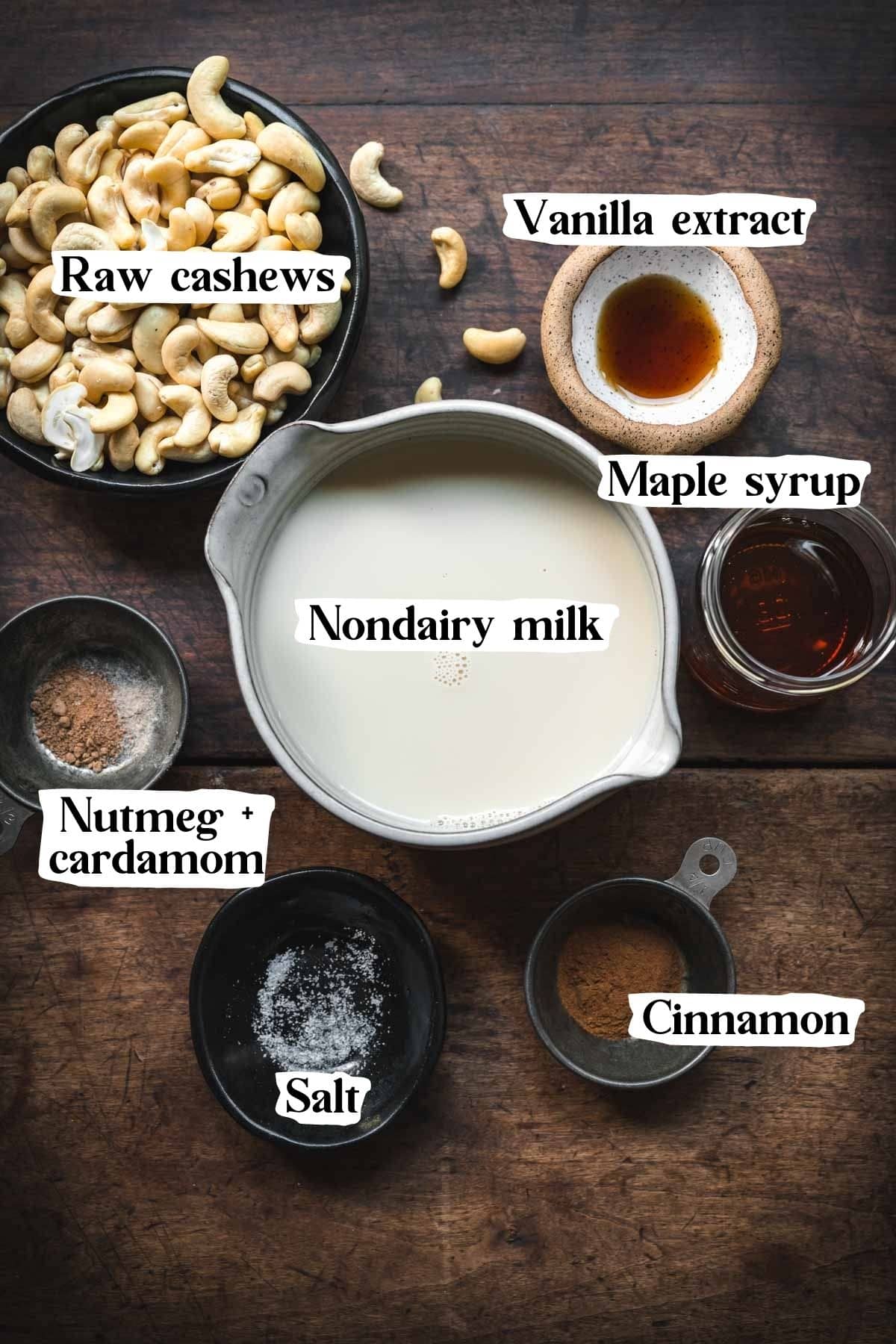 Overhead view of vegan eggnog ingredients, including cashews, vanilla extract, milk, maple, nutmeg, salt and cinnamon.