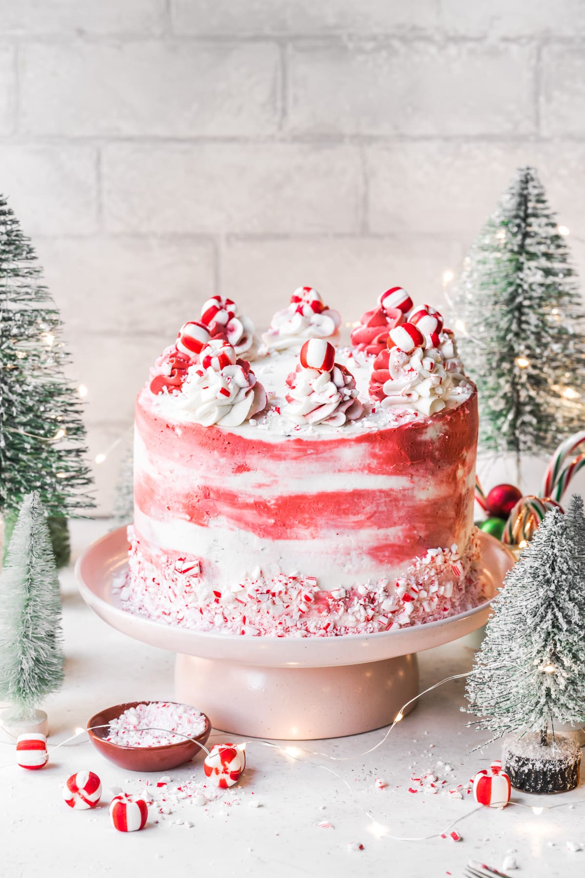 side view of vegan chocolate peppermint cake with red and white frosting with festive holiday props. 