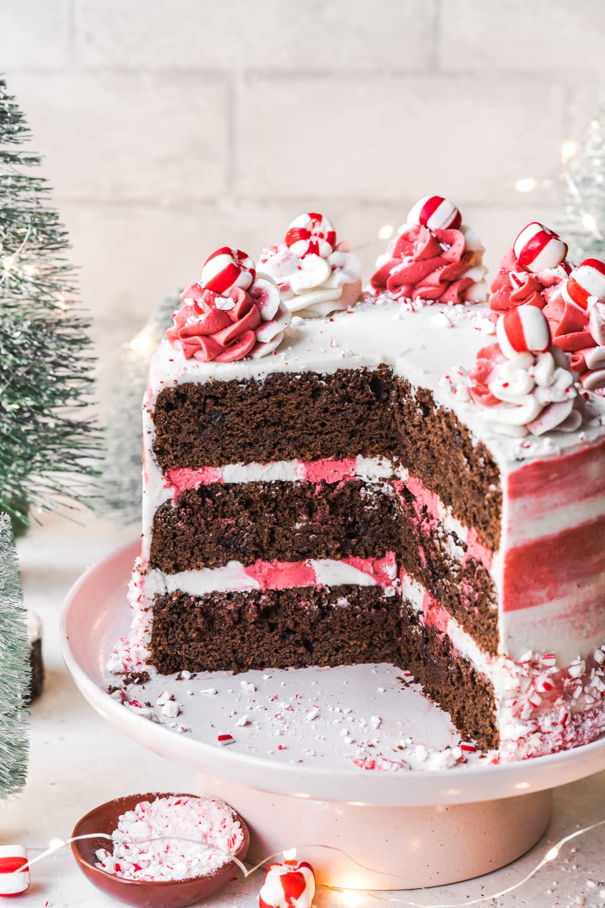 side view of vegan chocolate peppermint cake with red and white frosting with festive holiday props. 