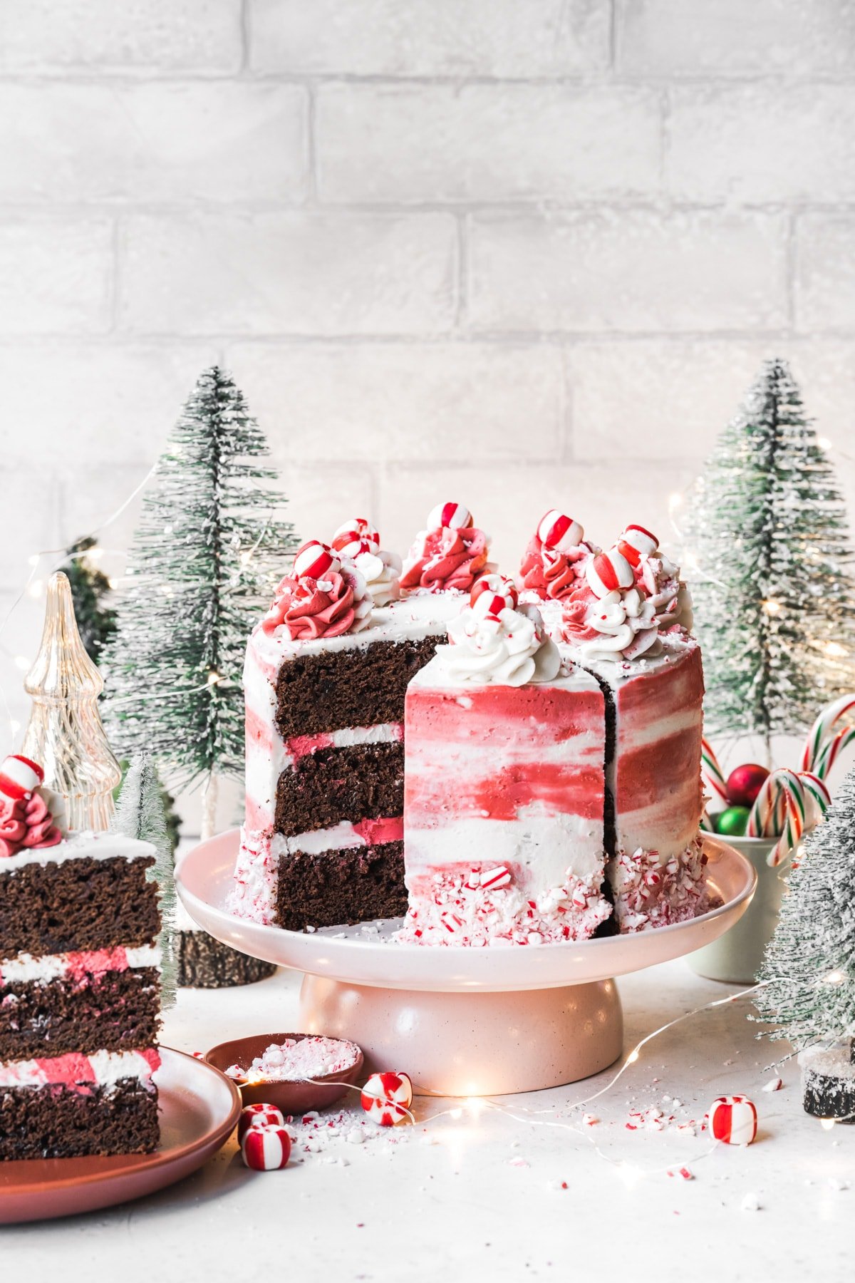 side view of vegan chocolate peppermint cake with red and white frosting with festive holiday props. 