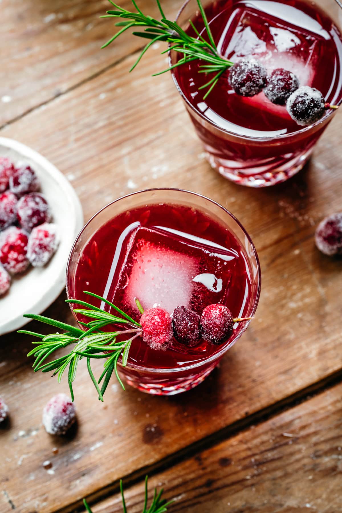 close up view of Christmas Old Fashioned cocktail with sugared cranberry and rosemary garnish. 