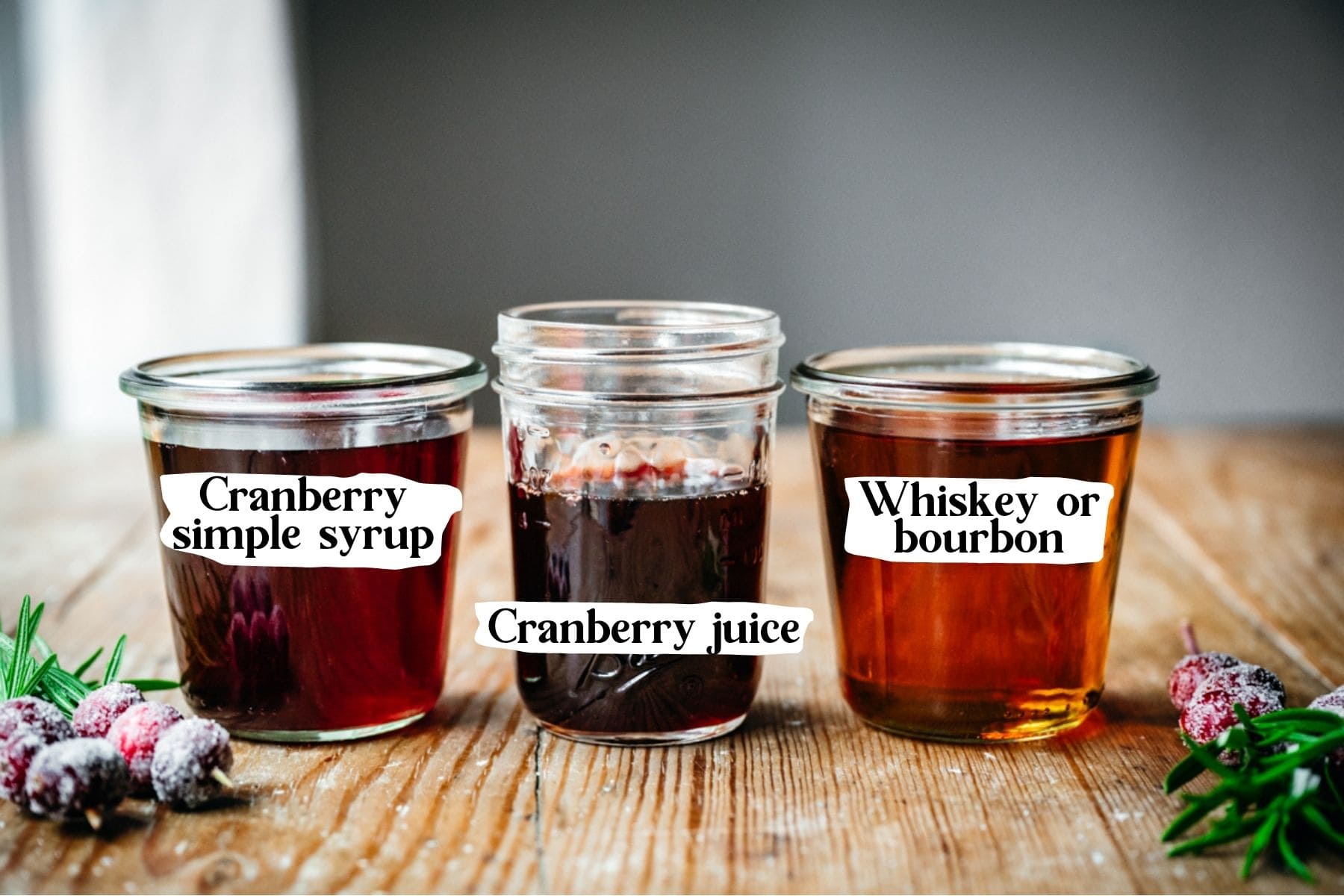 Front view of Christmas old fashioned ingredients, including cranberry simple syrup, cranberry juice, and whiskey.