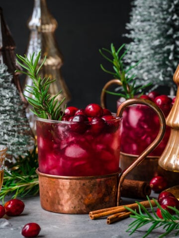 Front view of cranberry moscow mule garnished with cranberries and rosemary.