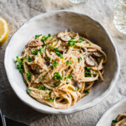 Close up view of vegan carbonara pasta garnished with parmesan and parsley in white bowl.