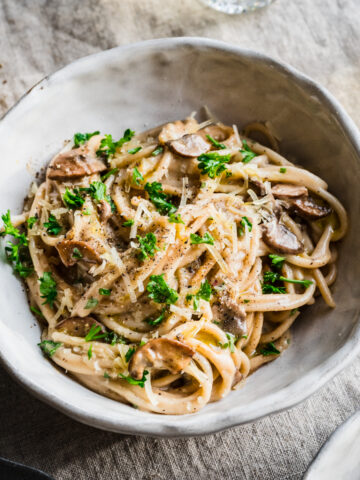 Close up view of vegan carbonara pasta garnished with parmesan and parsley in white bowl.