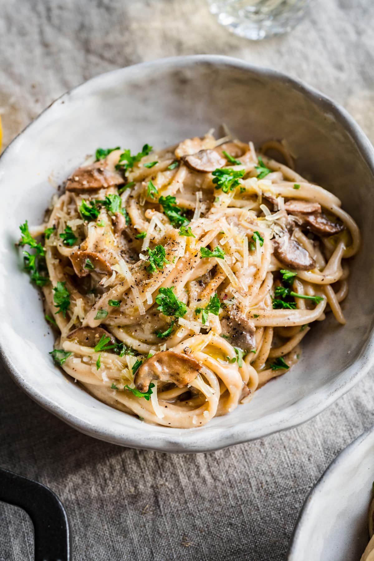 Close up view of vegan carbonara pasta garnished with parmesan and parsley in white bowl. 