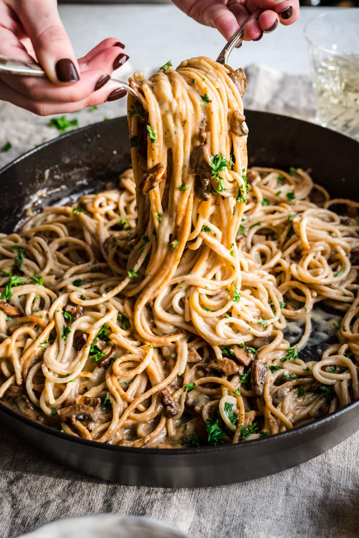 Person serving vegan carbonara pasta with two forks from large skillet. 