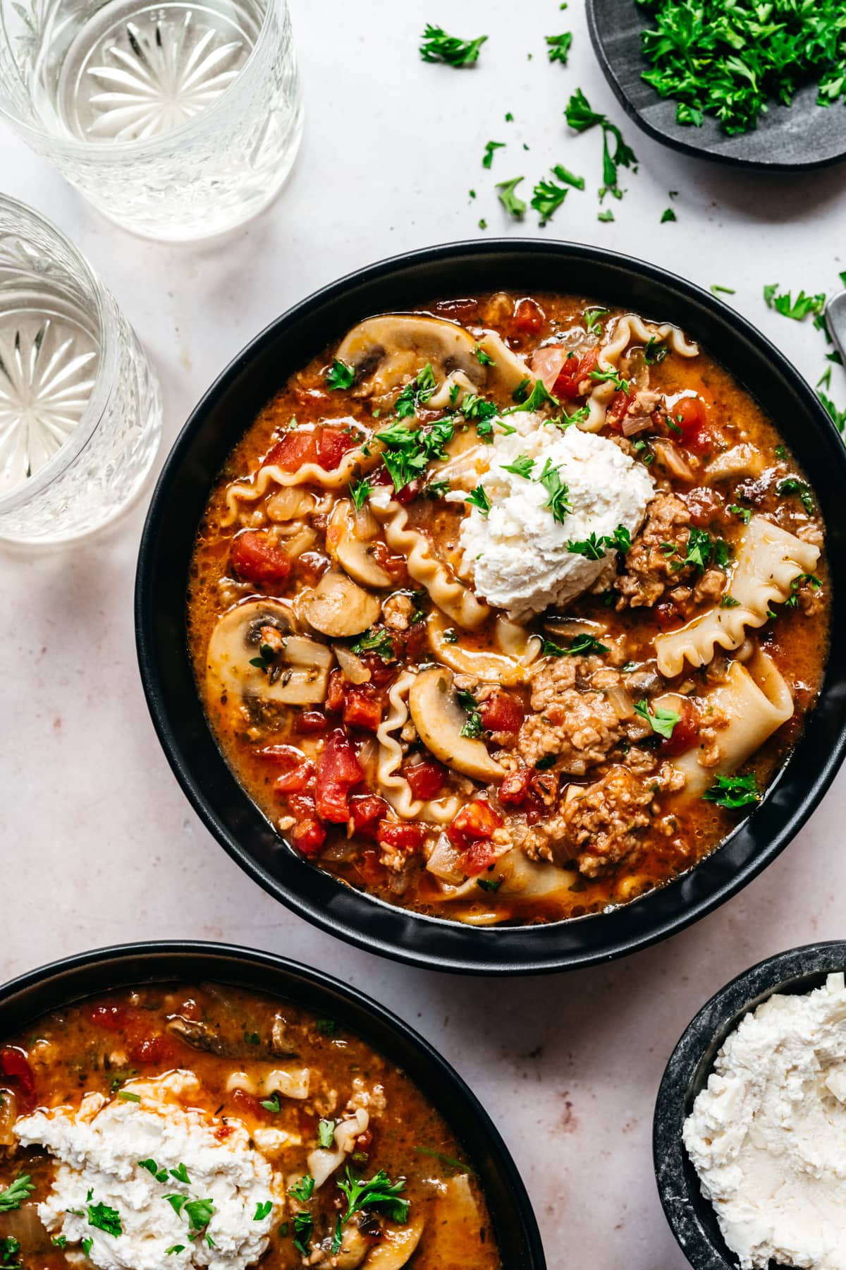 Overhead view of vegan lasagna soup garnished with vegan cheese and herbs.