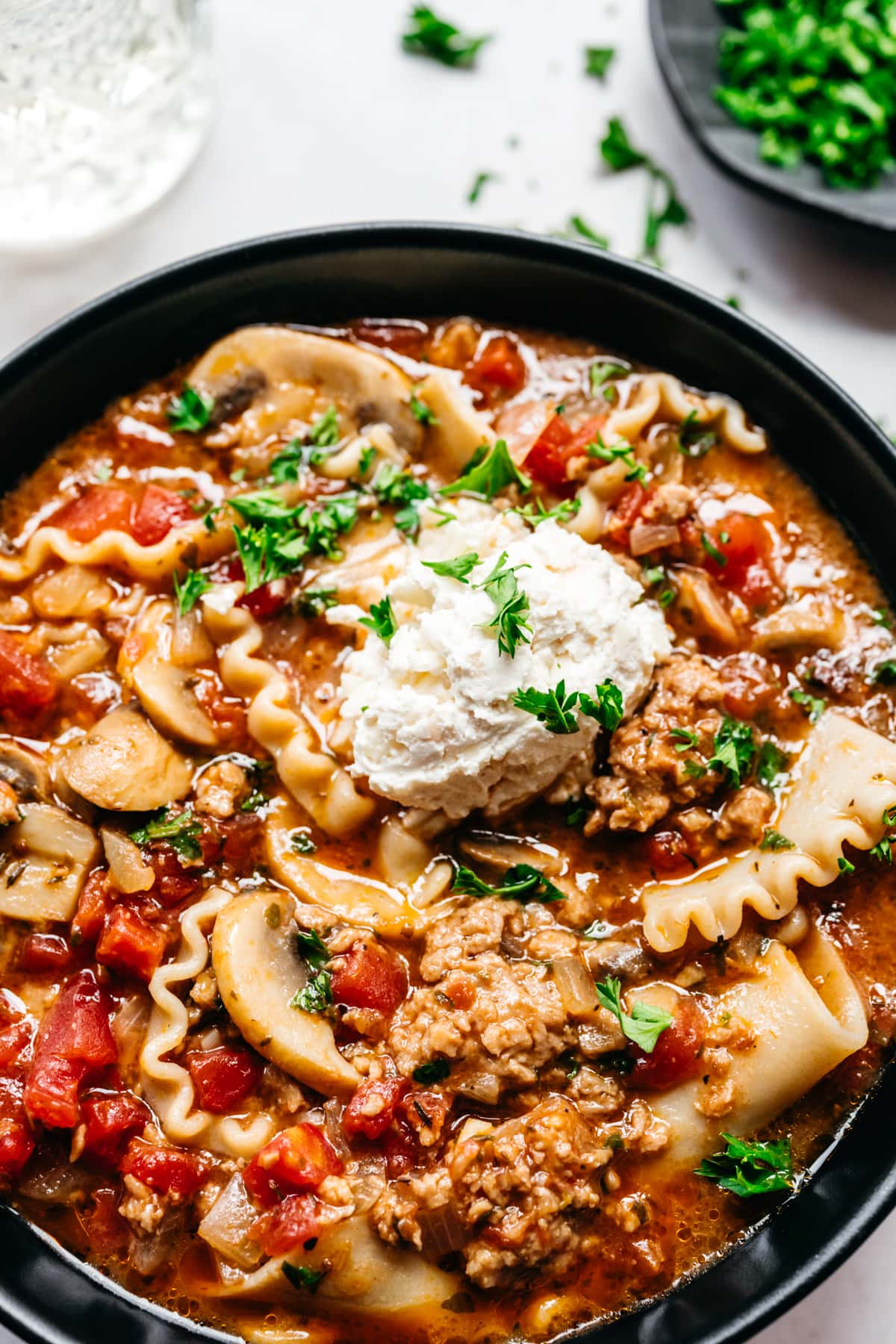 Close up view of vegan lasagna soup garnished with vegan cheese and herbs.