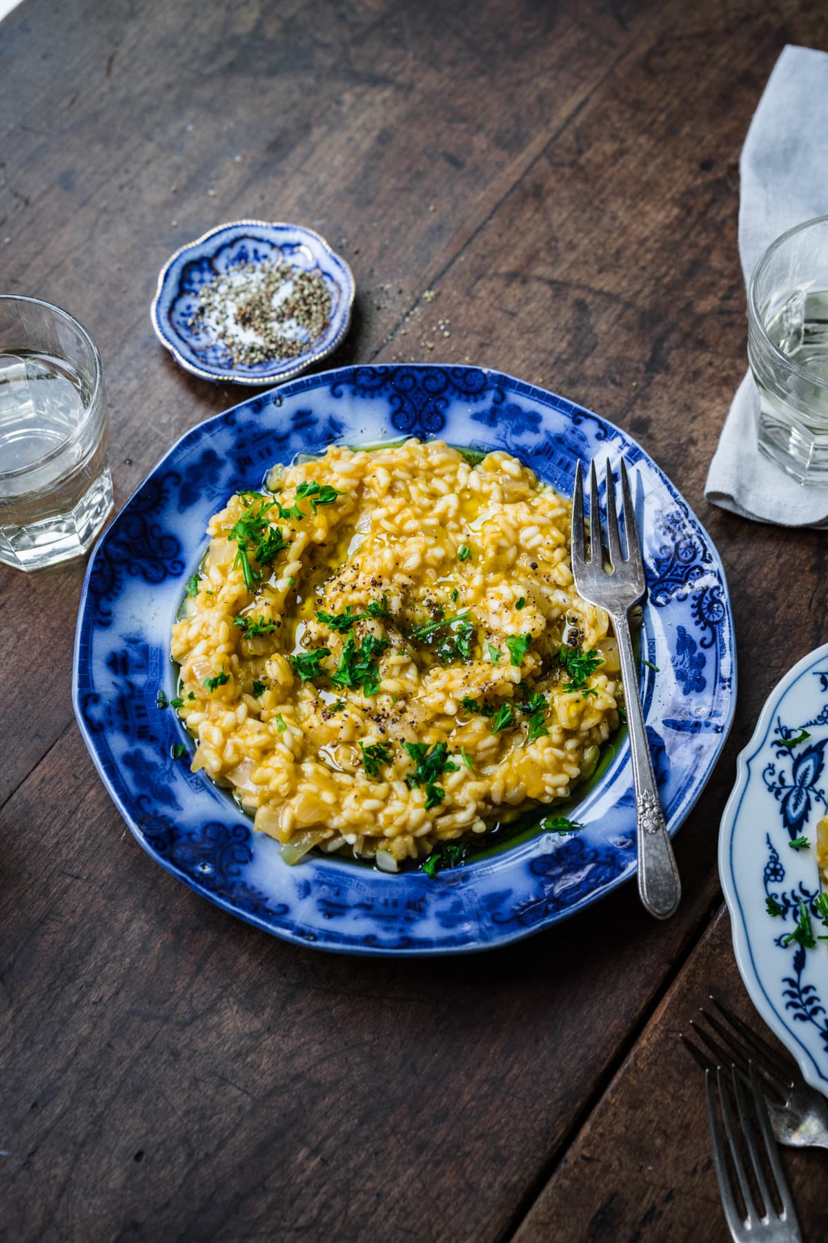 Vegan risotto in the middle of a table setting, with herbs and water nearby.