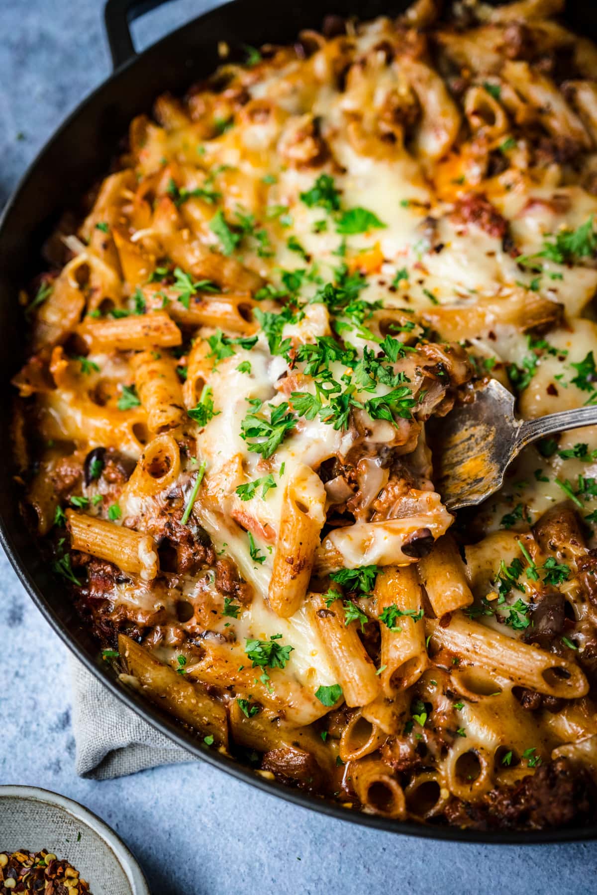 close up view of pasta al forno in skillet with serving spoon. 