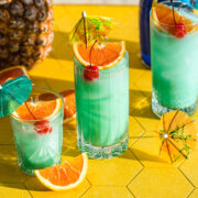 Front view of blue hawaiian cocktail garnished with orange and a cocktail umbrella.