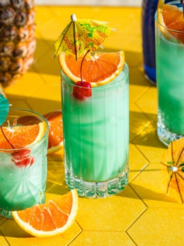 Front view of blue hawaiian cocktail garnished with orange and a cocktail umbrella.