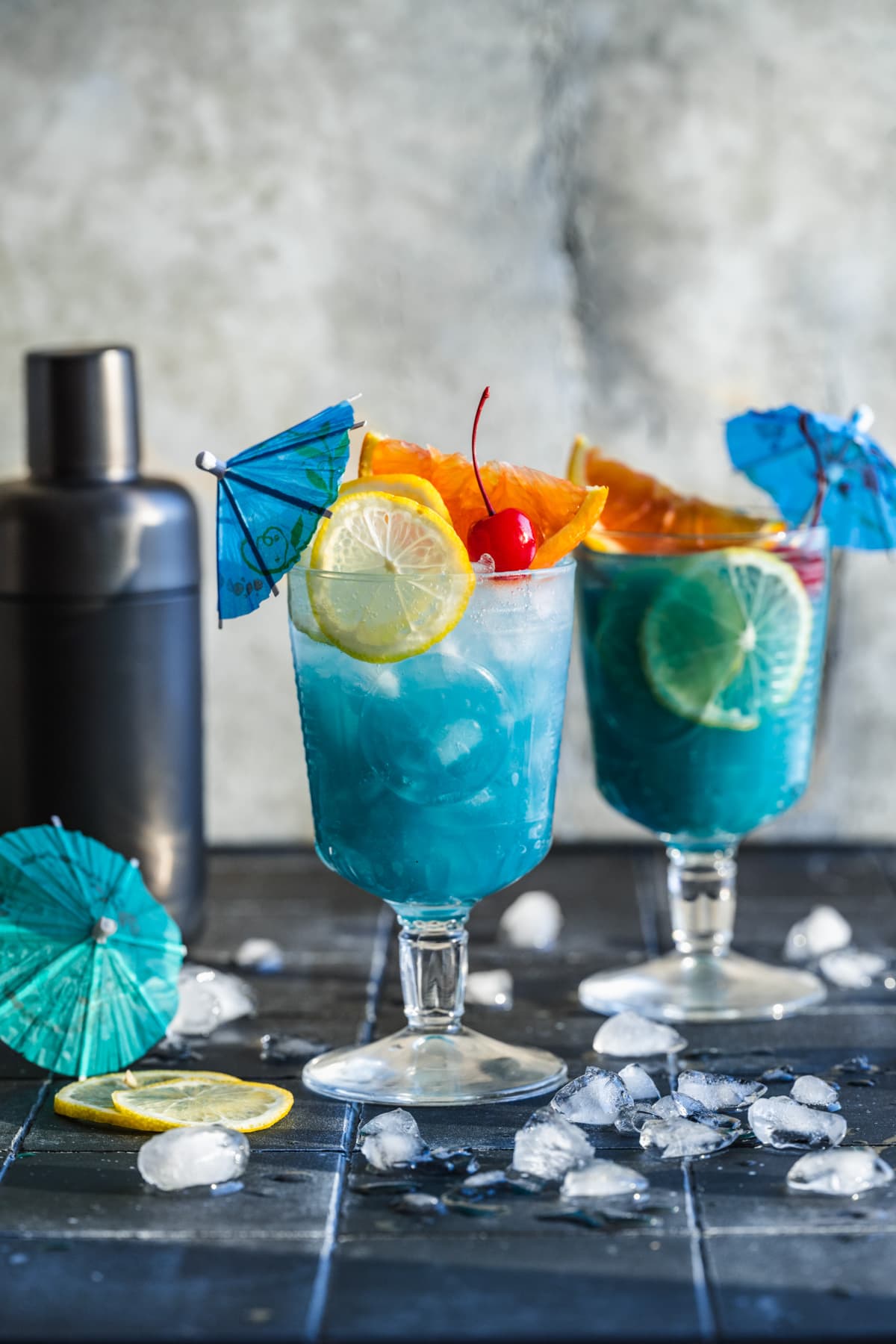 Side view of Blue Lagoon mocktail in goblet glass with cocktail umbrella and citrus slices. 