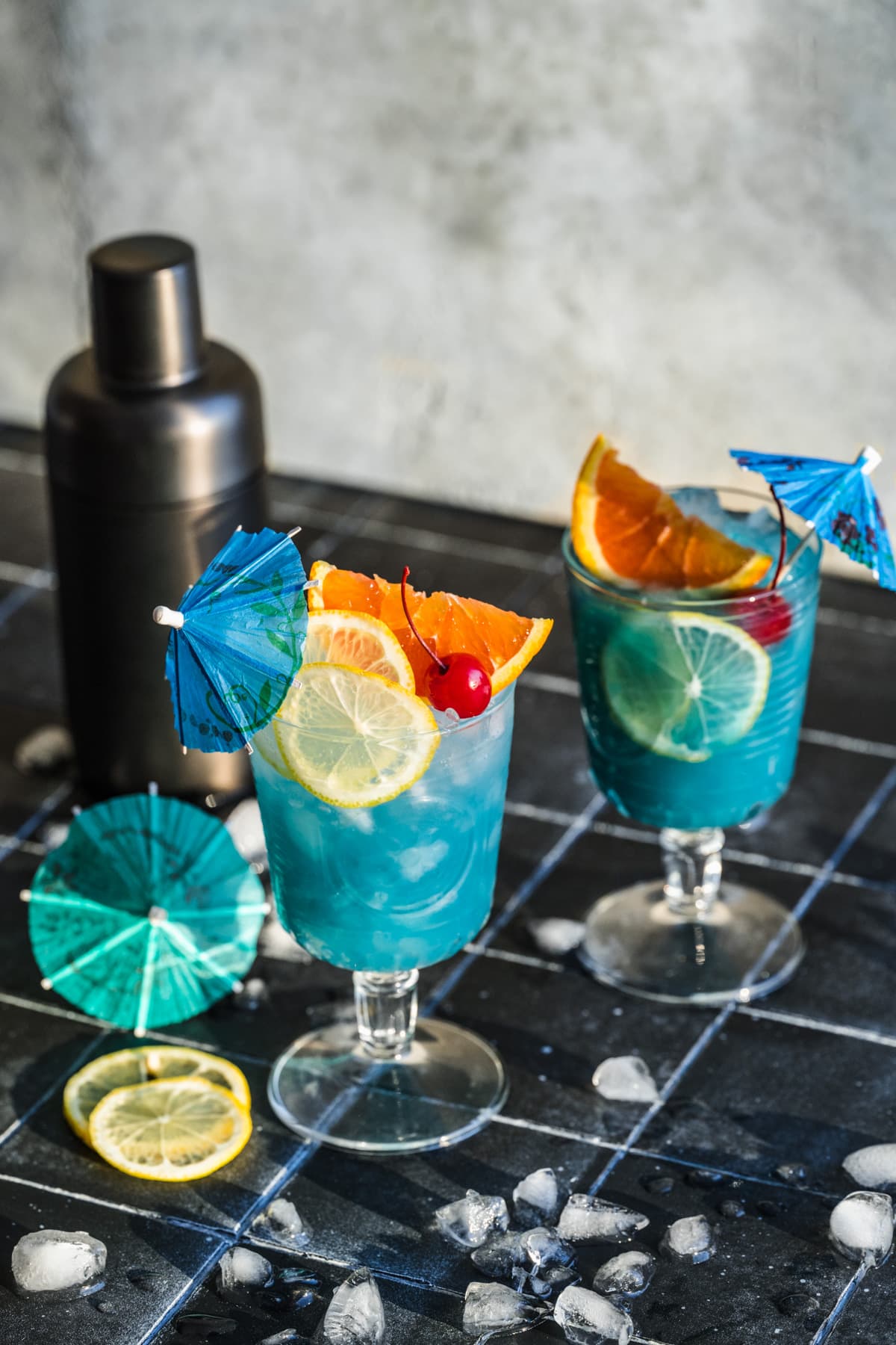 Side view of Blue Lagoon mocktail in goblet glass with cocktail umbrella and citrus slices. 
