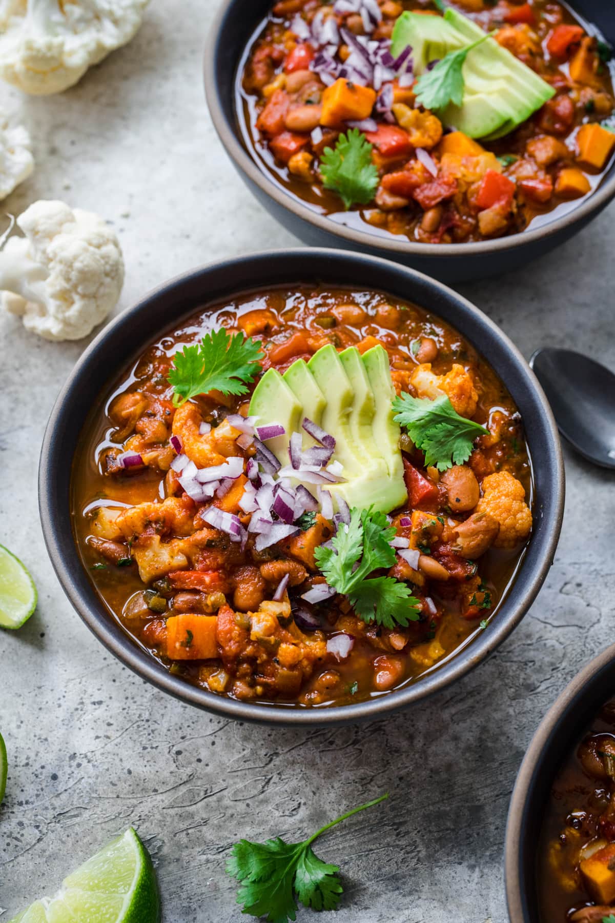 overhead view of bowl of vegan cauliflower chili topped with avocado and red onion. 