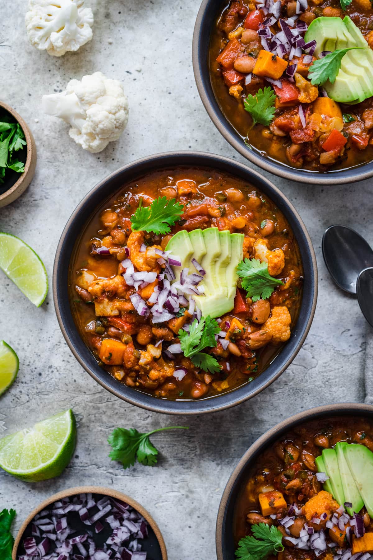 overhead view of bowl of vegan cauliflower chili topped with avocado and red onion. 