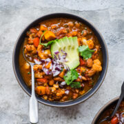 overhead view of bowl of vegan cauliflower chili topped with avocado and red onion.