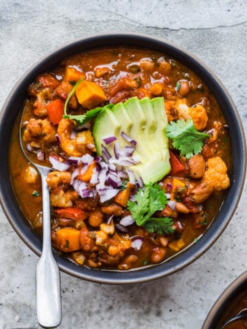 overhead view of bowl of vegan cauliflower chili topped with avocado and red onion.