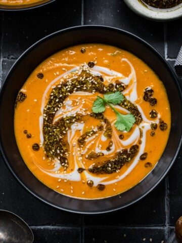 Overhead view of spicy carrot and lentil soup in black bowl on black tile.