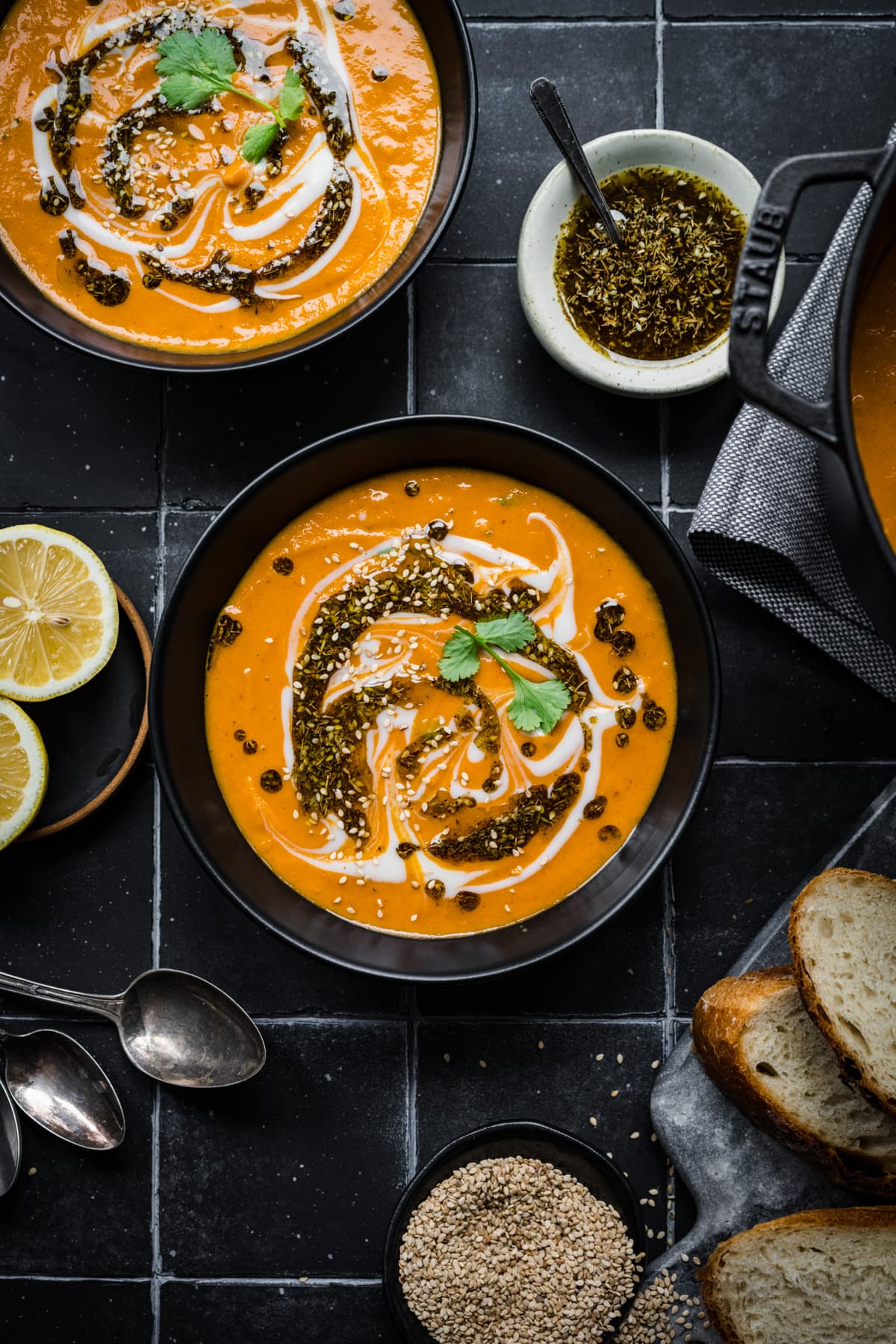 Overhead view of spicy carrot and lentil soup in black bowls on black tile. 