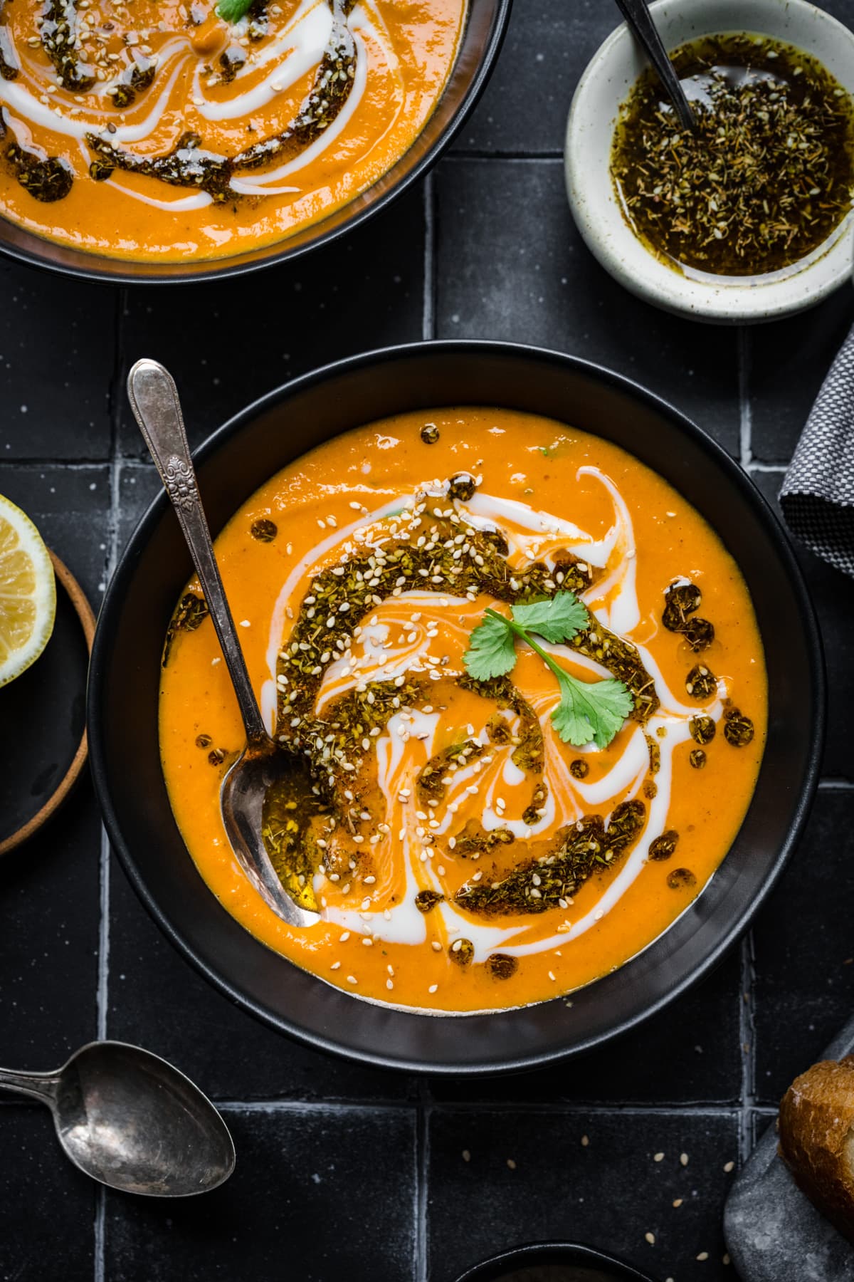 Overhead view of spicy carrot and lentil soup in black bowl on black tile. 