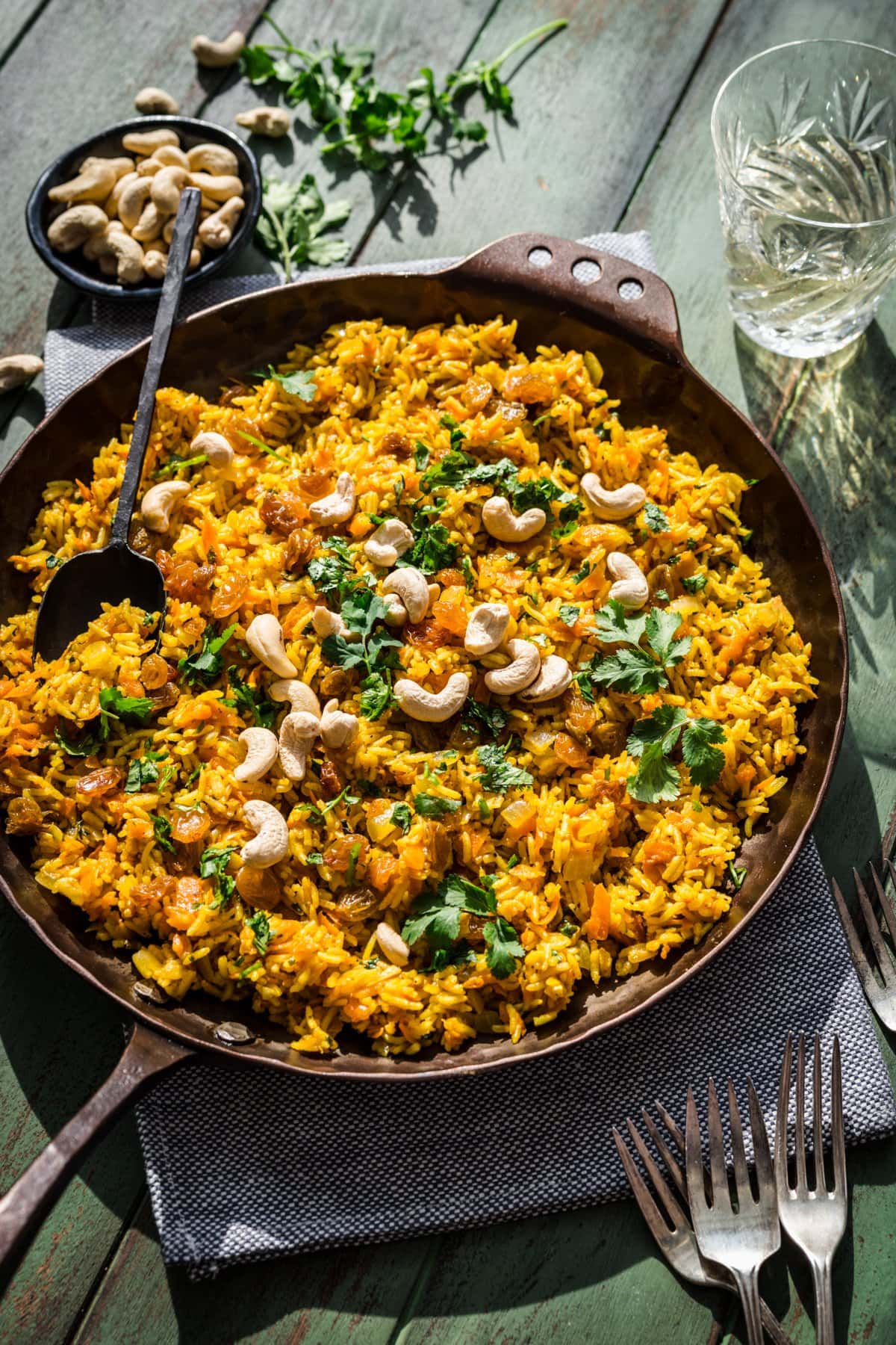Overhead view of carrot rice in a pan, garnished with golden raisins, cilantro, and cashews.