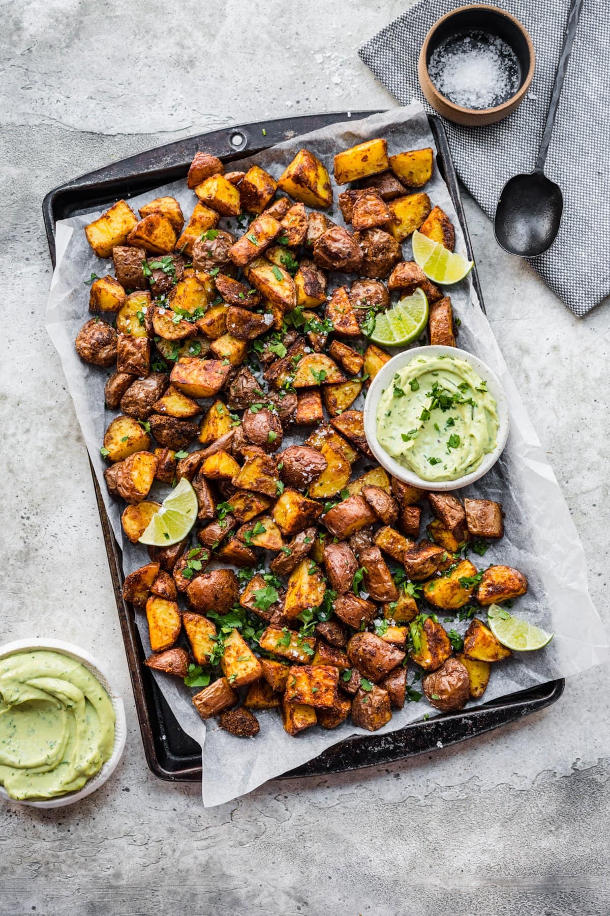 Overhead view of roasted mexican potatoes on a tray with an avocado crema.
