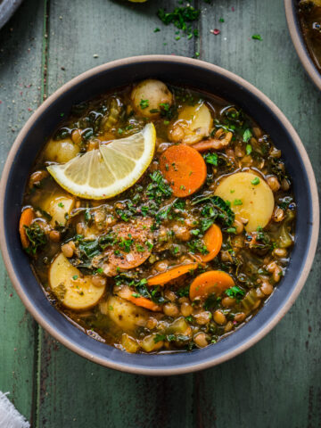 Overhead view of a bowl of potato lentil soup garnished with a lemon wedge.