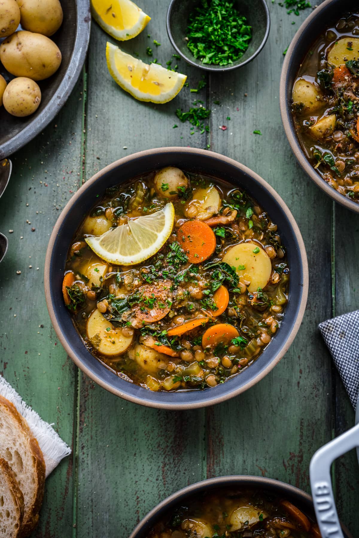 Overhead view of potato lentil soup in a bowl, garnished with a lemon wedge and herbs.