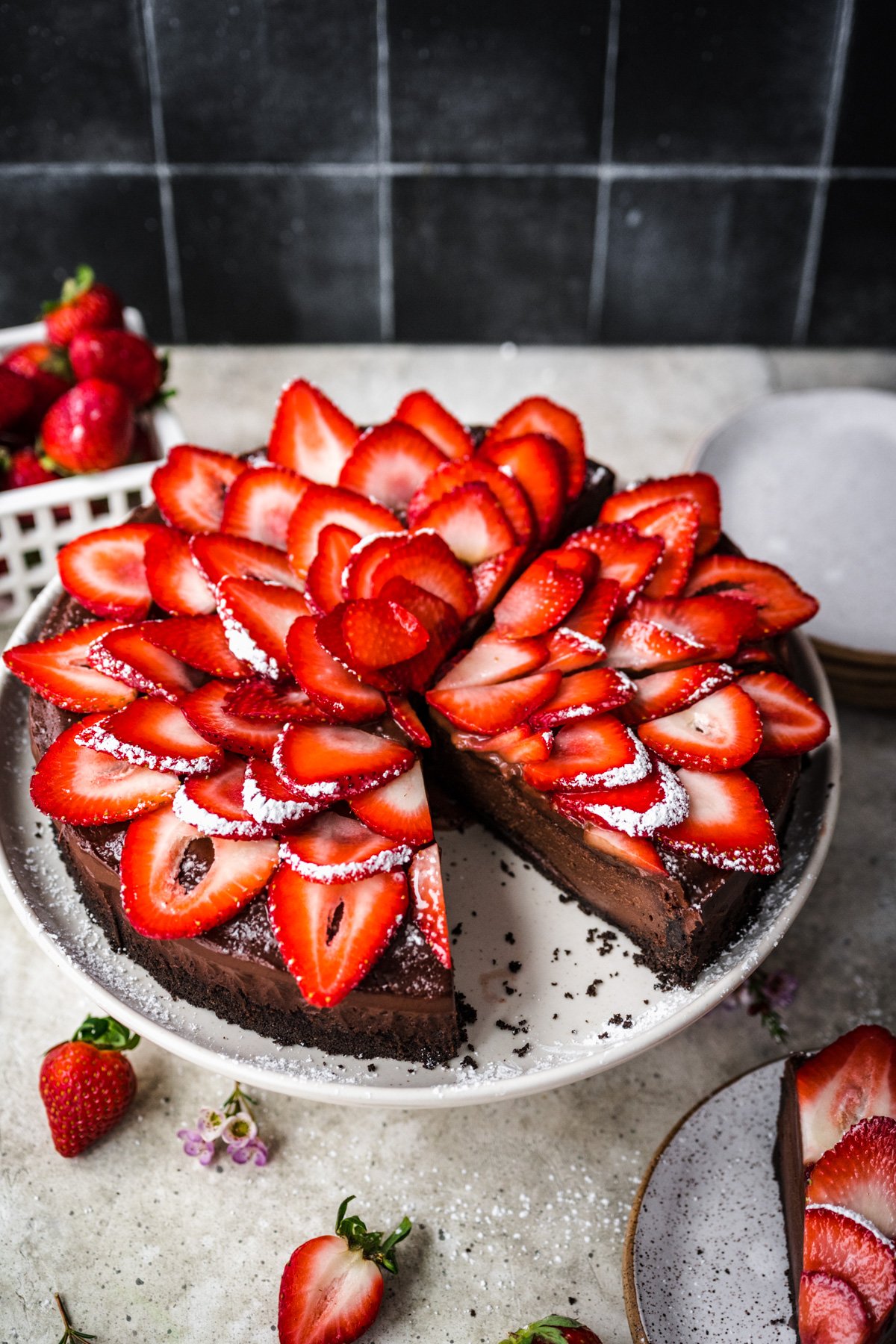 vegan chocolate cheesecake topped with strawberries on cake platter. 