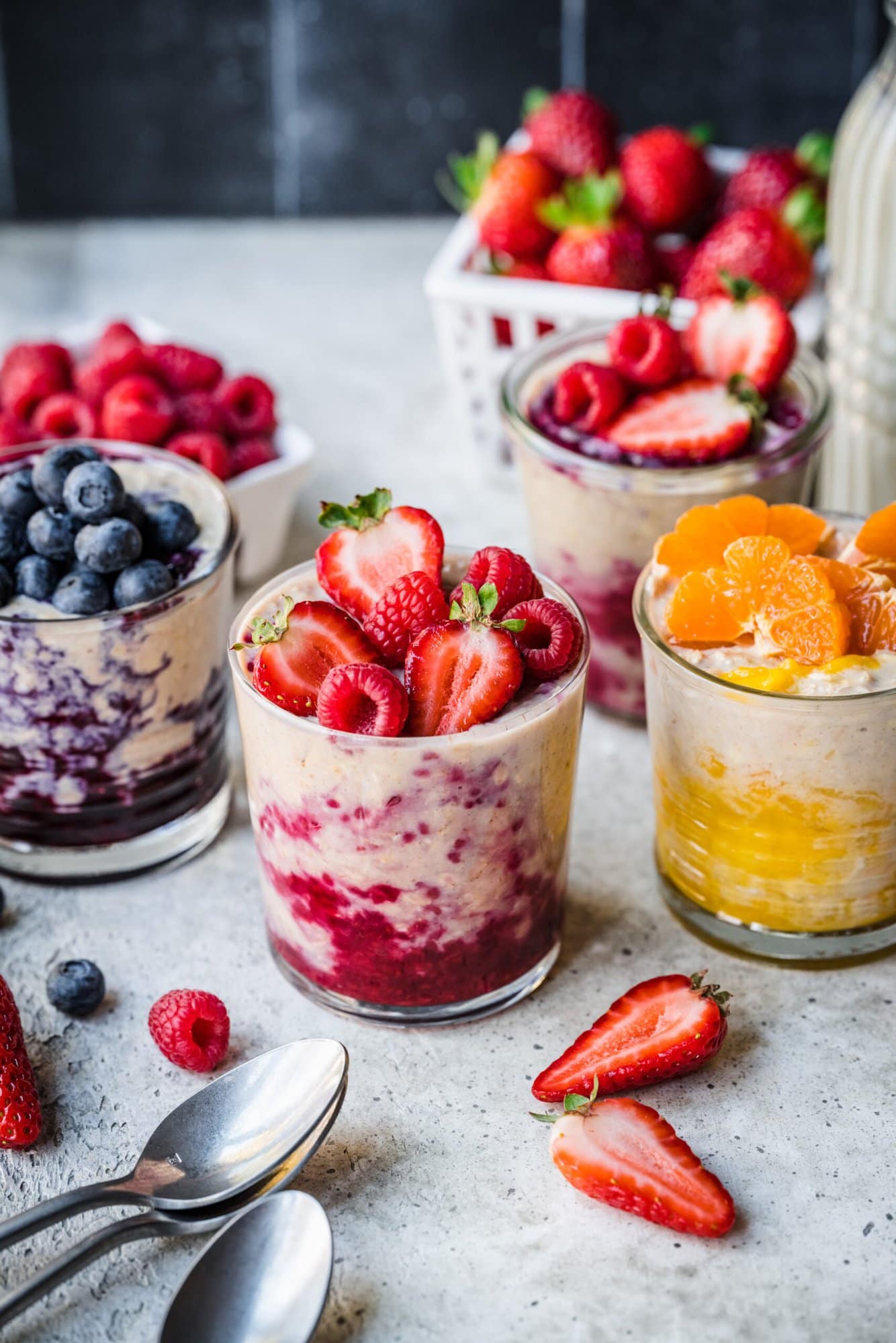 Protein overnight oats in glass jars with berry compote and fresh fruit on top. 