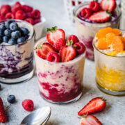 Protein overnight oats in glass jars with berry compote and fresh fruit on top.
