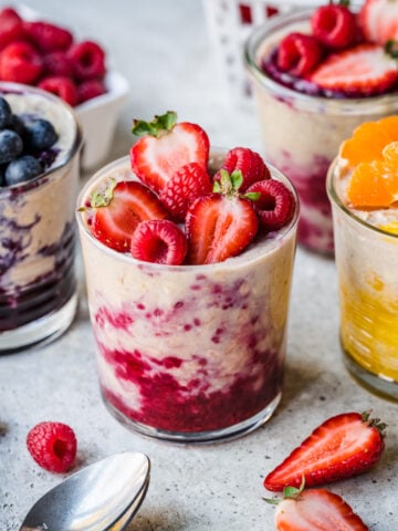 Protein overnight oats in glass jars with berry compote and fresh fruit on top.