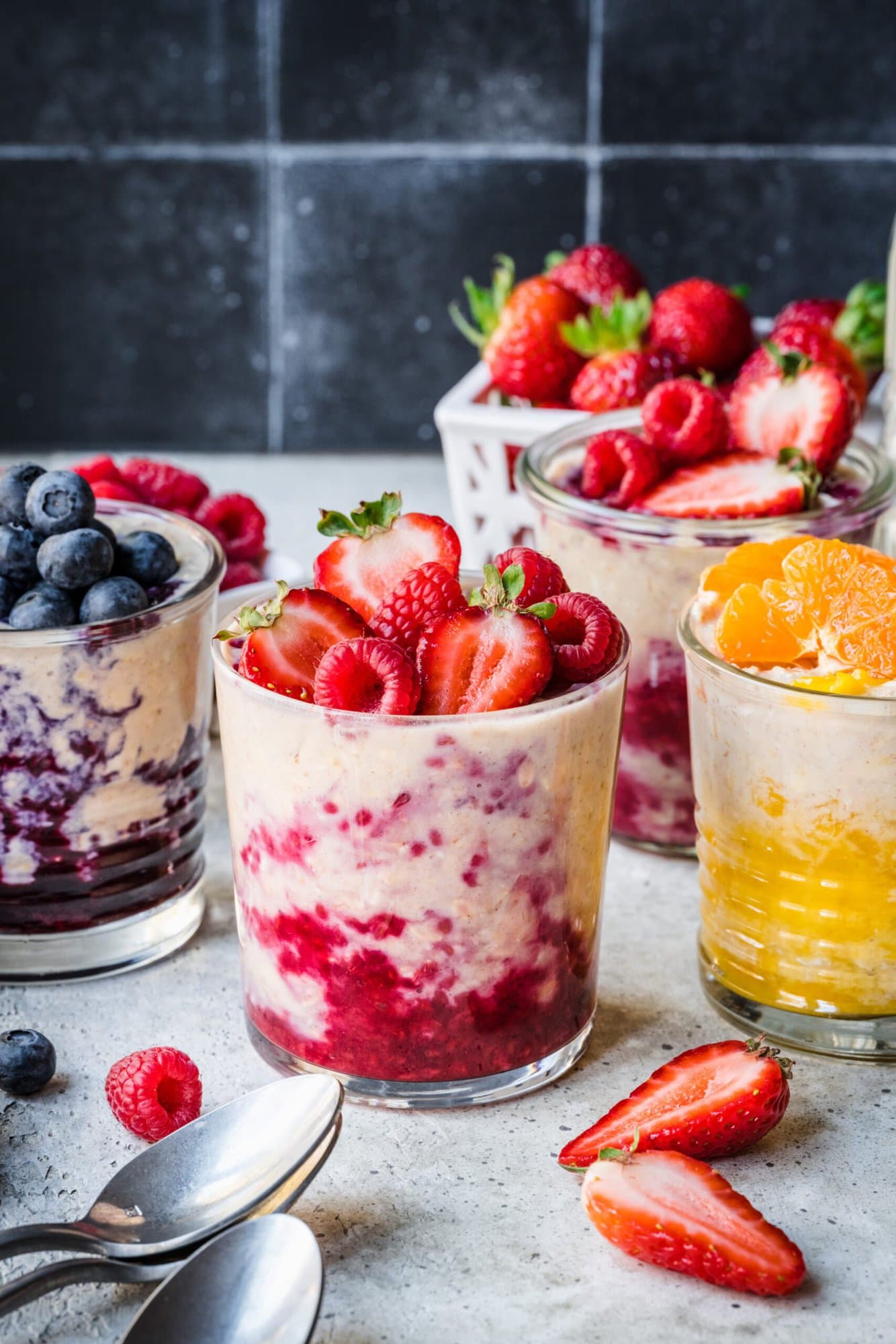 Protein overnight oats in glass jars with berry compote and fresh fruit on top. 