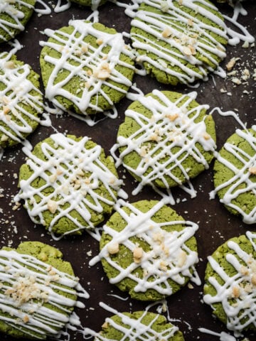 Overhead view of vegan matcha cookies with white chocolate drizzle on baking sheet.