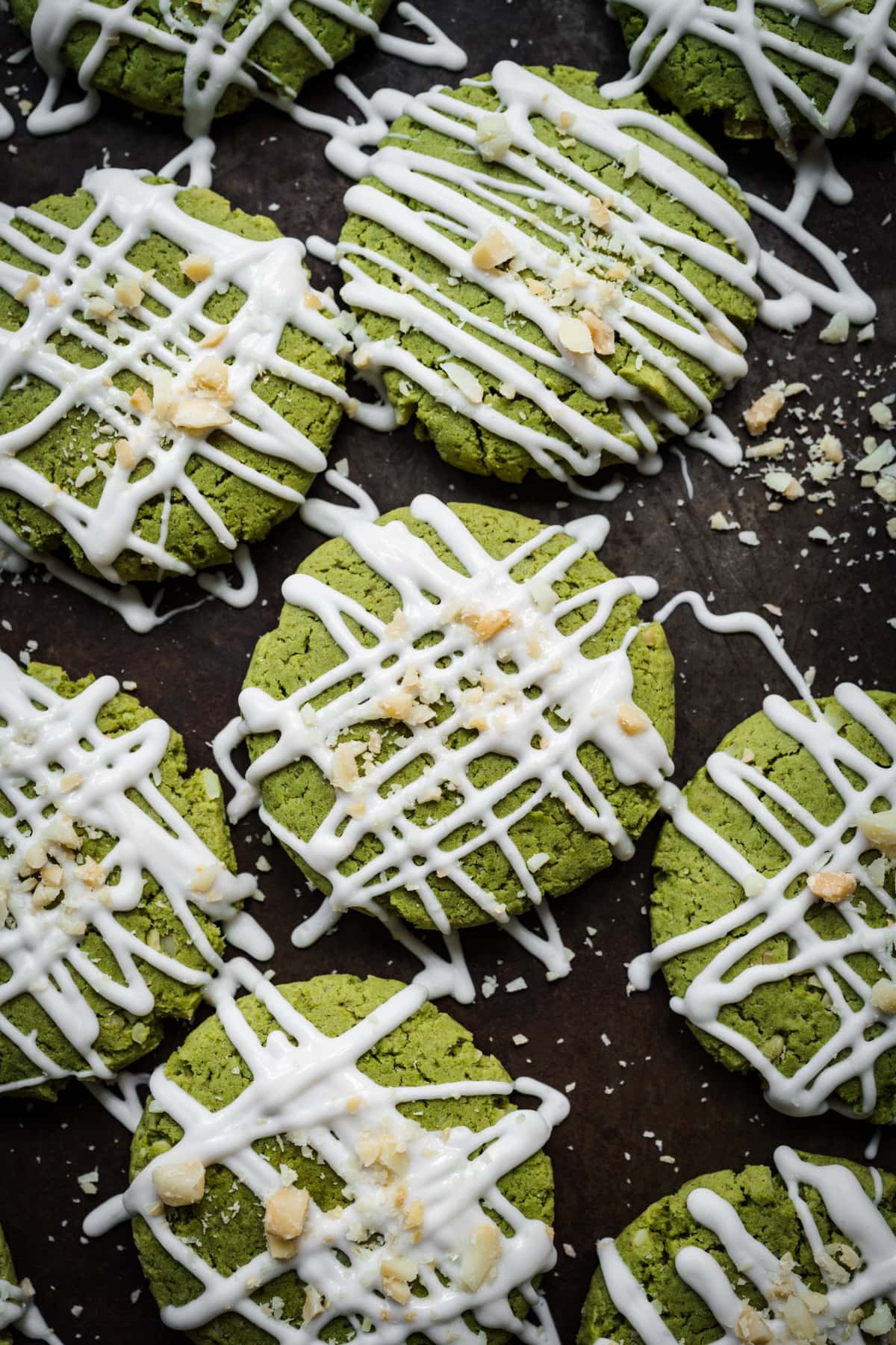 Overhead view of vegan matcha cookies with white chocolate drizzle on baking sheet.