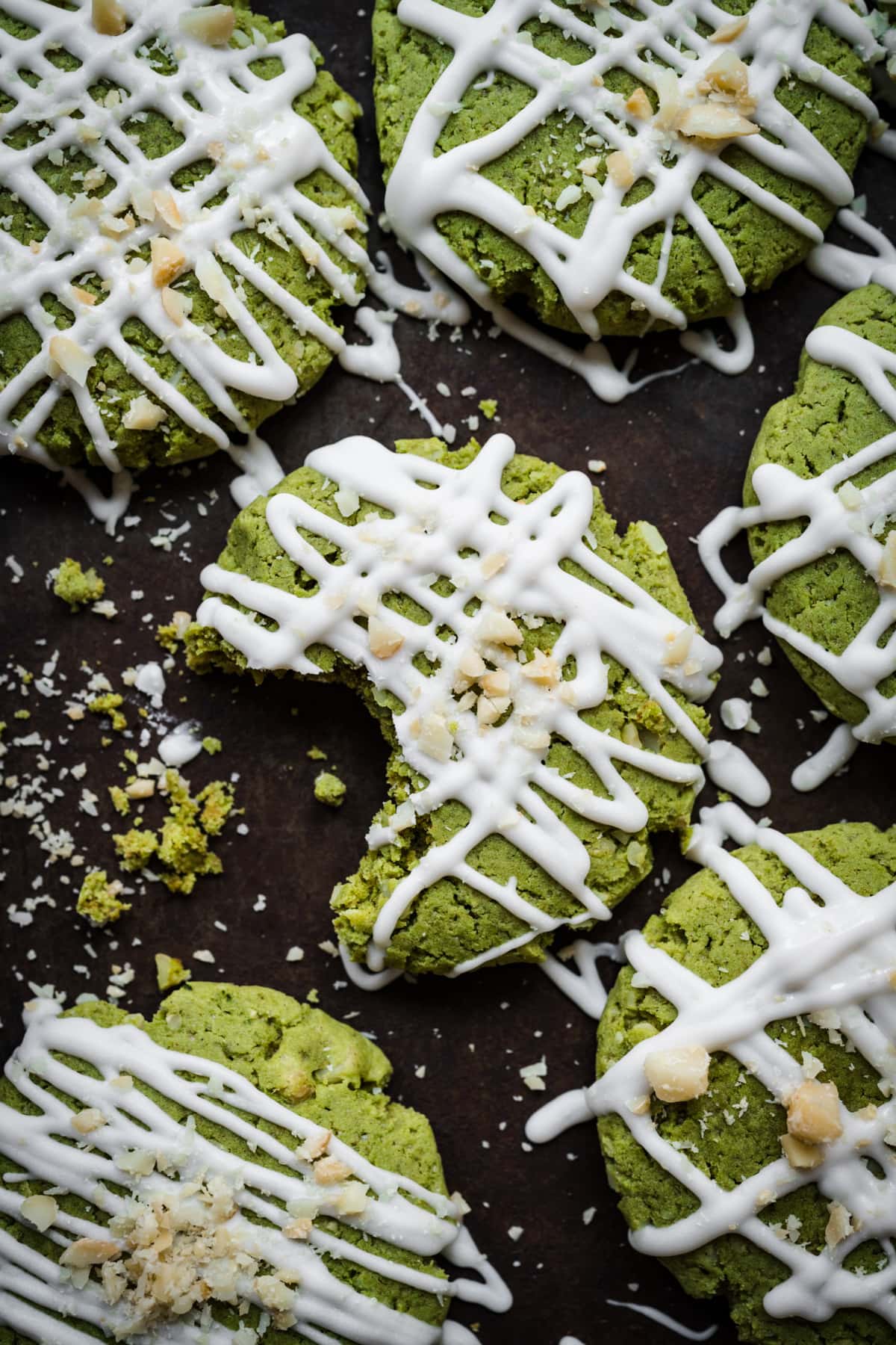 Overhead view of vegan matcha cookies with white chocolate drizzle with bite taken out of one cookie. 