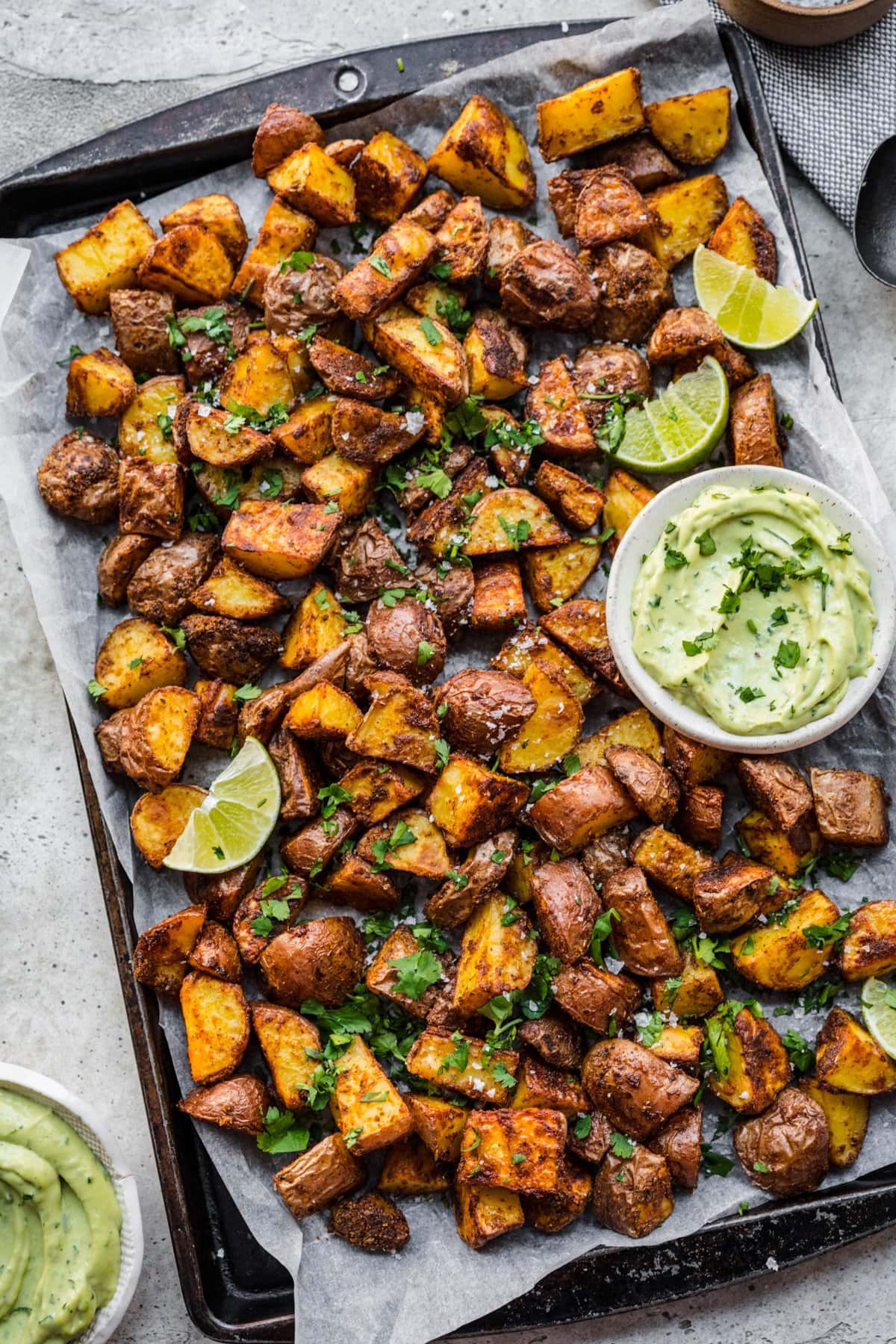 Overhead view of roasted mexican potatoes on a tray with an avocado crema.