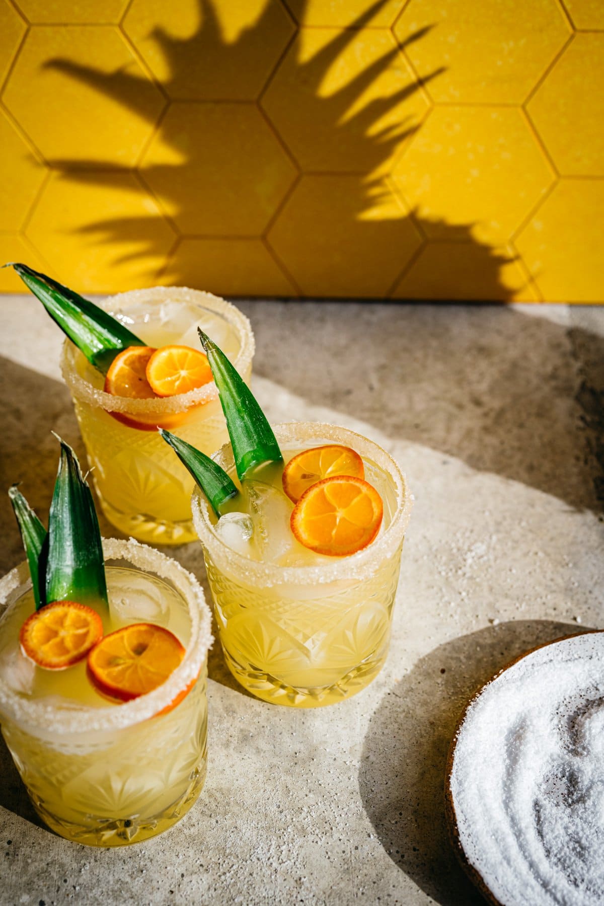 Side view of pineapple margarita in salt rimmed glass with yellow backdrop. 