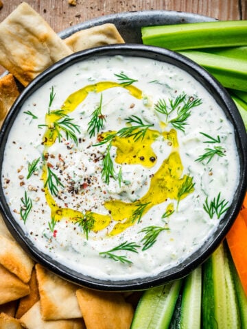 Vegan tzatziki in a bowl surrounded by veggies and chips.
