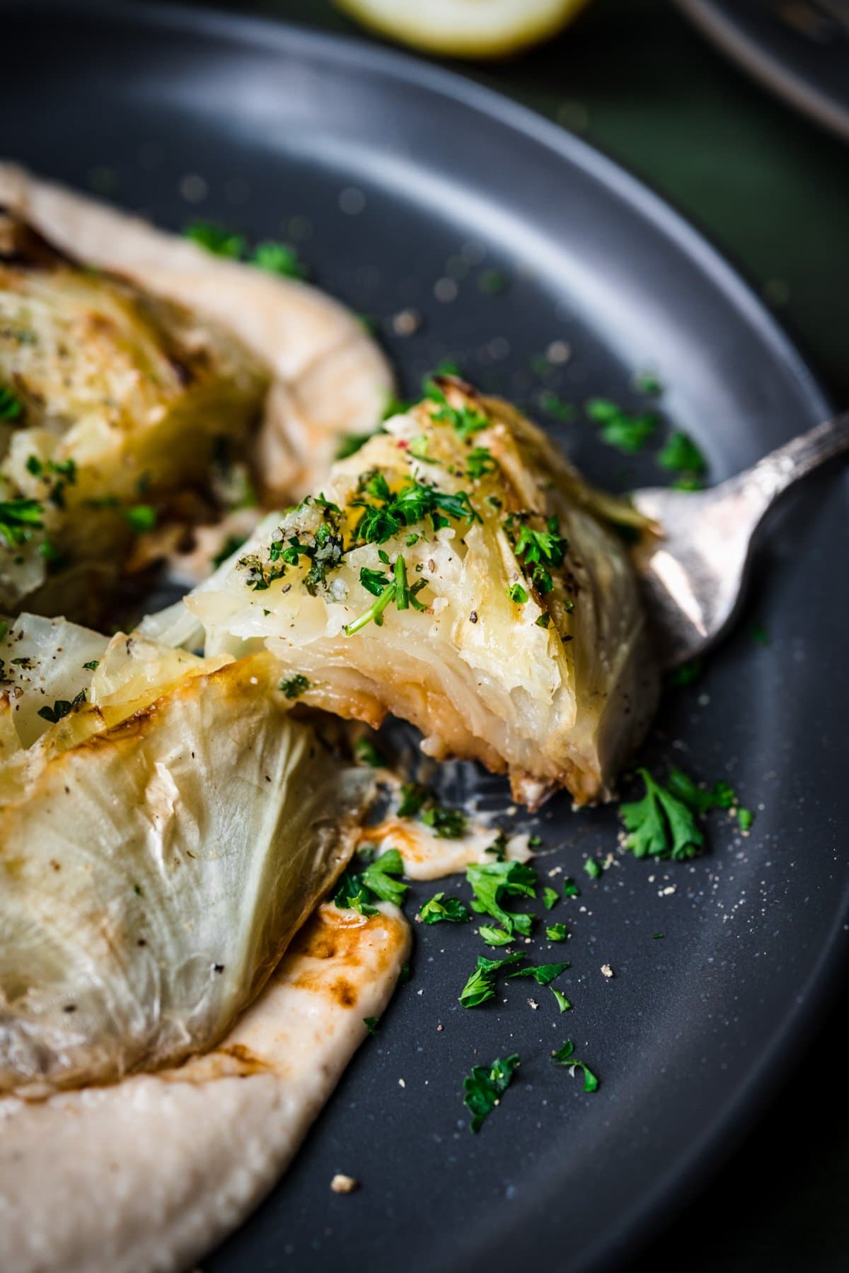 Cabbage steak slice on a fork over white bean puree. 