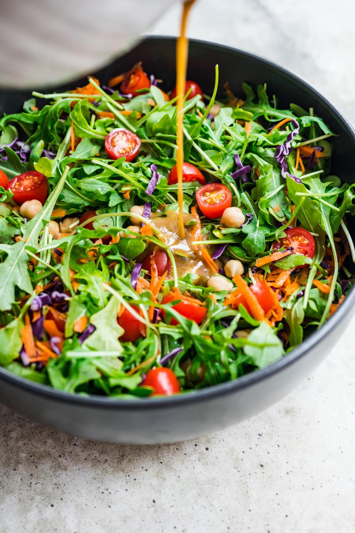 Front view of balsamic vinaigrette being poured over a green salad.