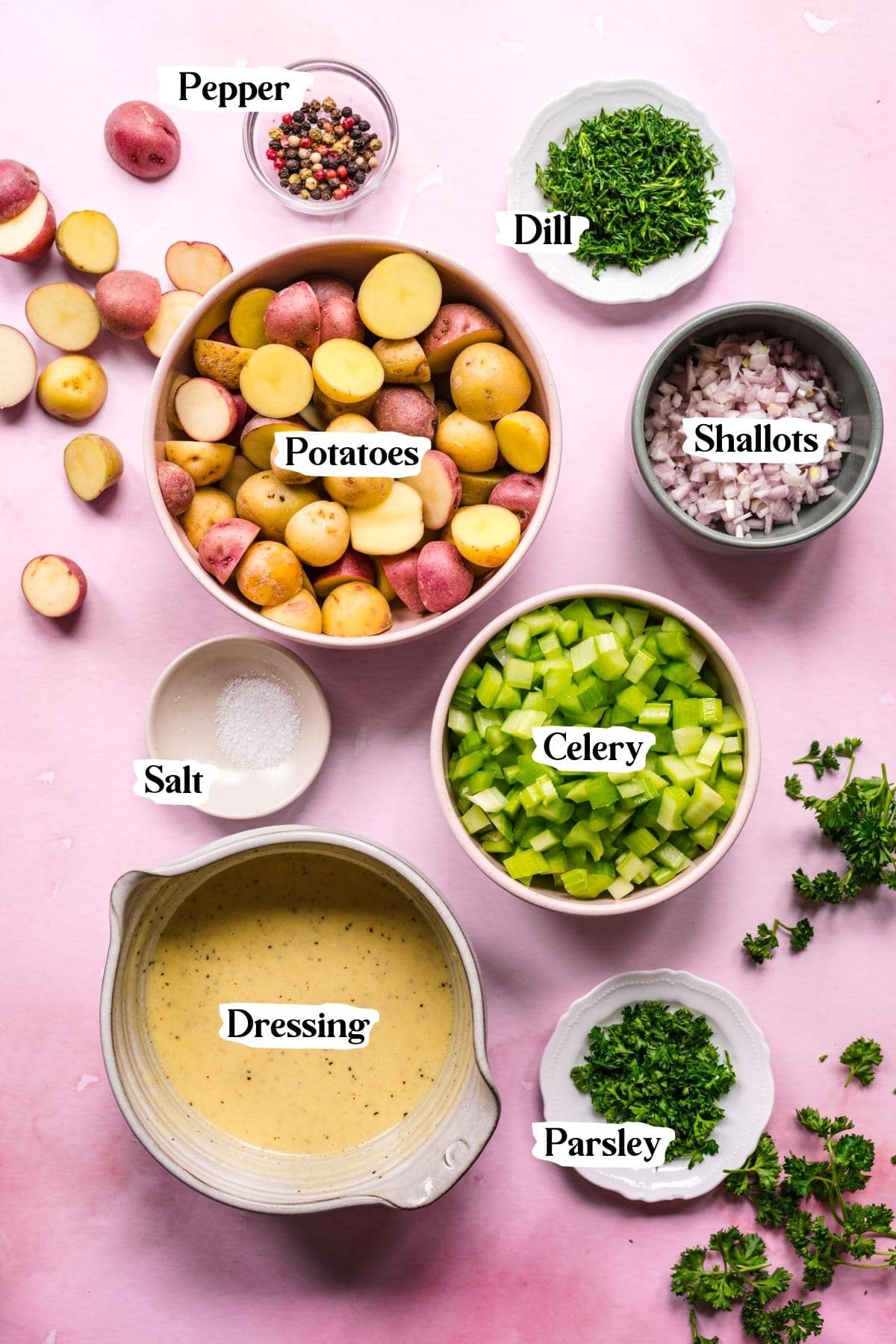 Overhead view of ingredients for dill potato salad in small prep bowls on pink backdrop.