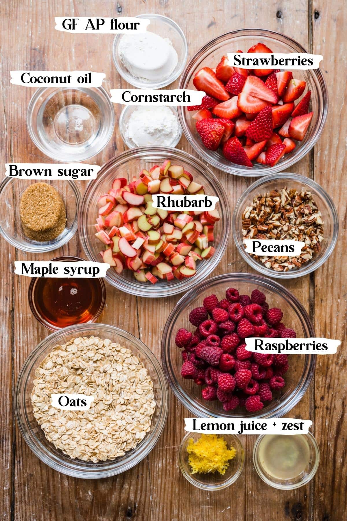 overhead view of ingredients for strawberry rhubarb crisp in small prep bowls with text labels. 