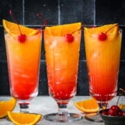 Front view of three tequila sunrise mocktails with cherry garnish.