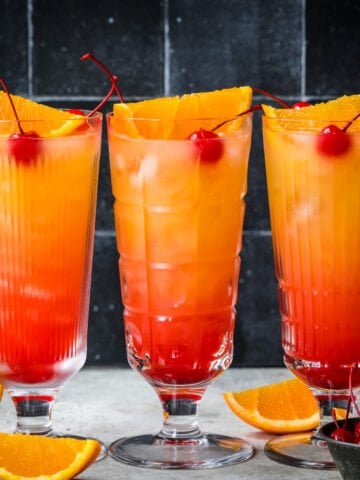 Front view of three tequila sunrise mocktails with cherry garnish.