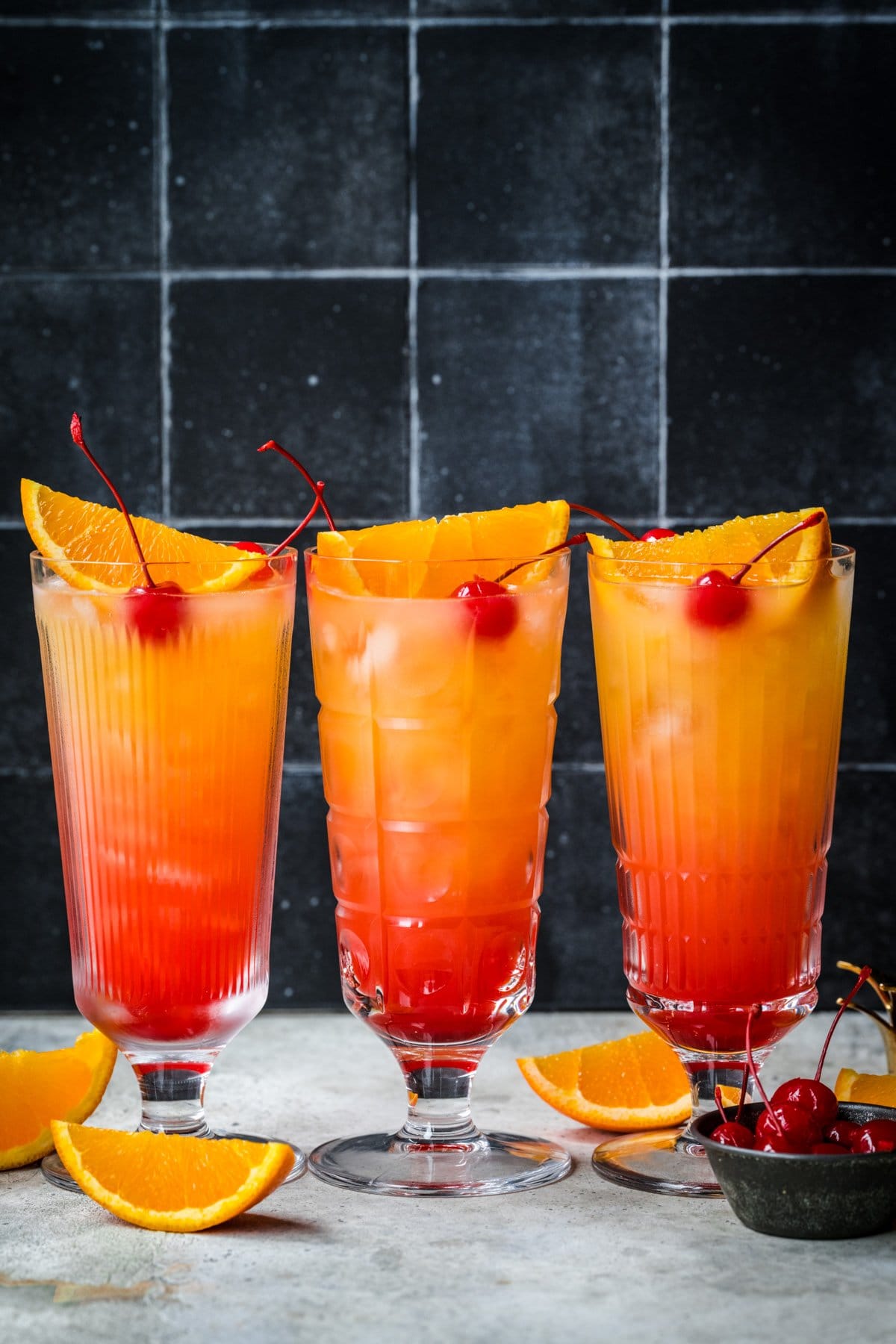 Front view of three tequila sunrise mocktails garnished with orange and cherry.