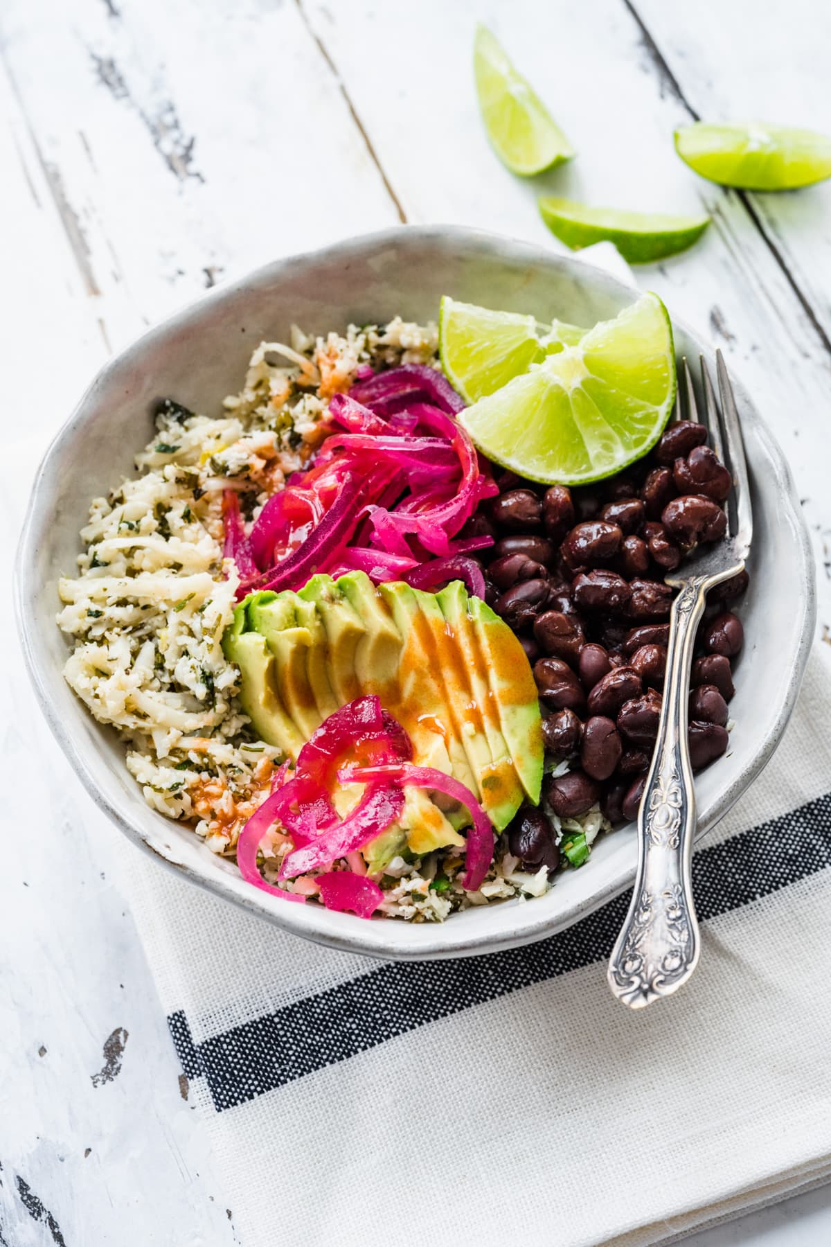 Close up view of cilantro lime cauliflower rice topped with avocado, pickled red onions, and black beans.